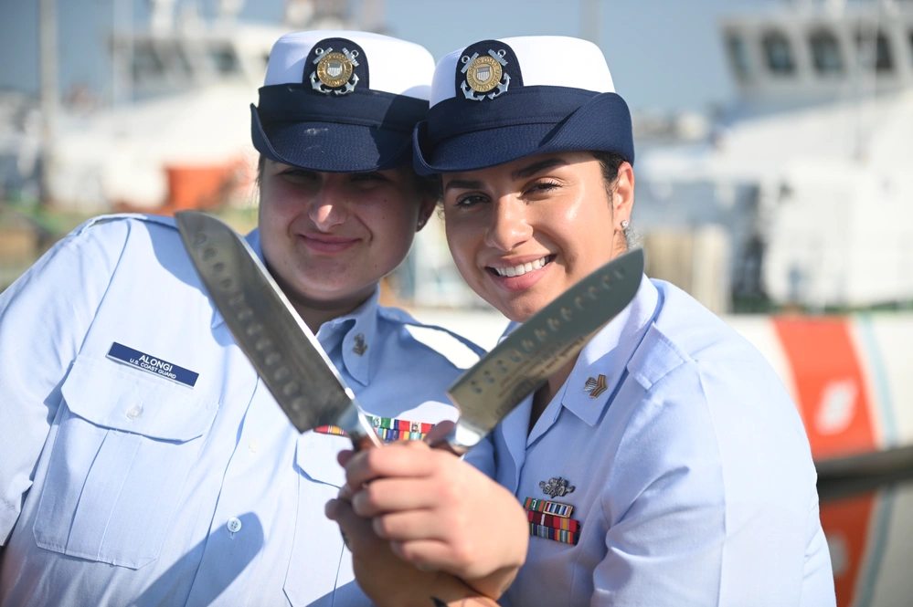 Petty Officer 2nd Class Gabriella Alongi and Petty Officer 1st Class Jennaya Allen pose with their newly acquired knives that read, “Thank you and YES CHEF!” which was gifted to them by Master Chief Petty Officer James Swenson, the rating force master chief for culinary specialists, during an advancement ceremony at Coast Guard Station Little Creek in Virginia Beach, Virginia, Aug. 26, 2024. The knives are an acknowledgment from the master chief of their achievements as culinary specialists and is a unique gift within the rating. (U.S. Coast Guard Photo by Petty Officer 2nd Class Ryan L. Noel)