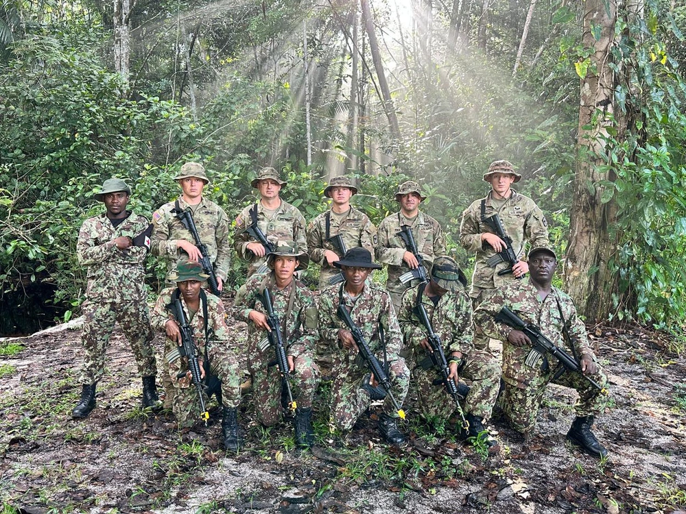 A group of soldiers holding rifles pose for a group photo in the jungle.
