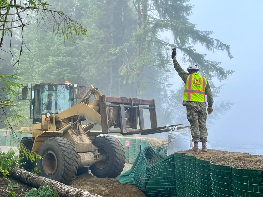 Command Sgt. Maj. Zachary Plummer assists the street team to repair a temporary flood protection barrier along the Mendenhall River