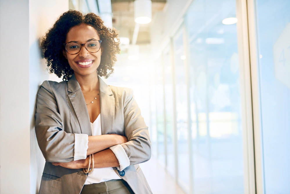 African american lady with glasses with arms crossed smiling in front of glass windows