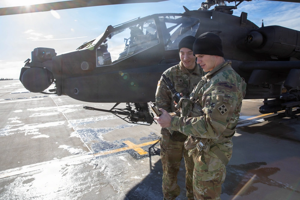 Spc. Joseph Hughes and 1st Lt. Andrew Bane, 4th Infantry Division, review mission data generated by the Android Team Awareness Kit beside an AH-64 Apache helicopter during Ivy Sting 4 at Fort Carson, Colorado, Jan. 28, 2026.