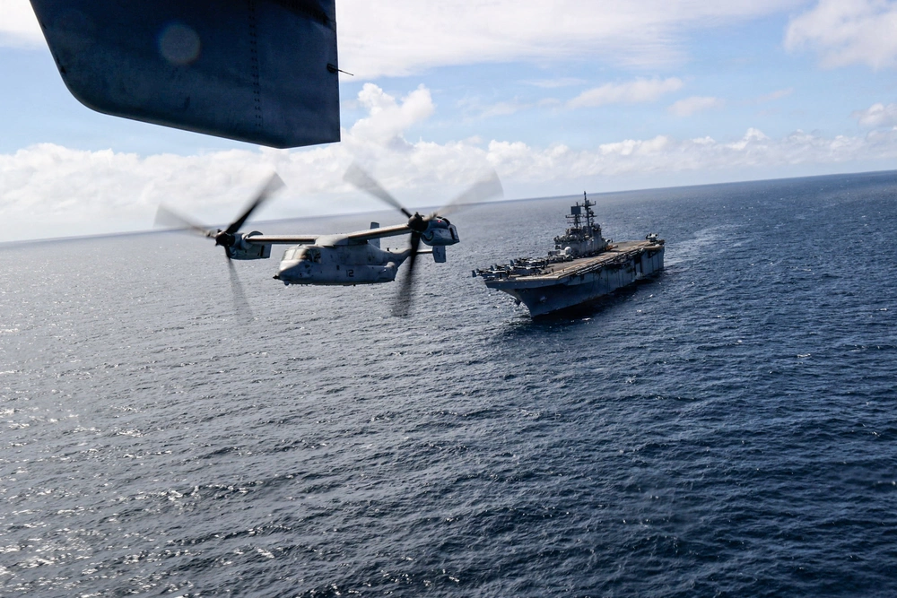 A military aircraft flies above a naval warship at sea.